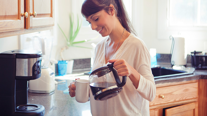 Une femme se sert une tasse de café avec une machine à café à filtre